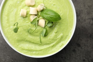 Photo of Tasty pea cream soup with croutons, basil and microgreens on grey table, top view