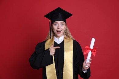 Photo of Happy student pointing at diploma after graduation on red background