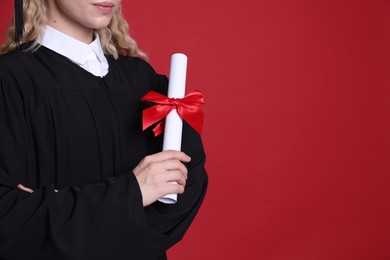 Photo of Student with diploma after graduation on red background, closeup. Space for text
