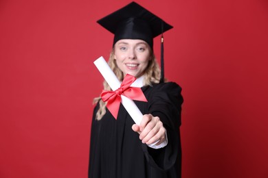 Photo of Happy student with diploma after graduation on red background, selective focus