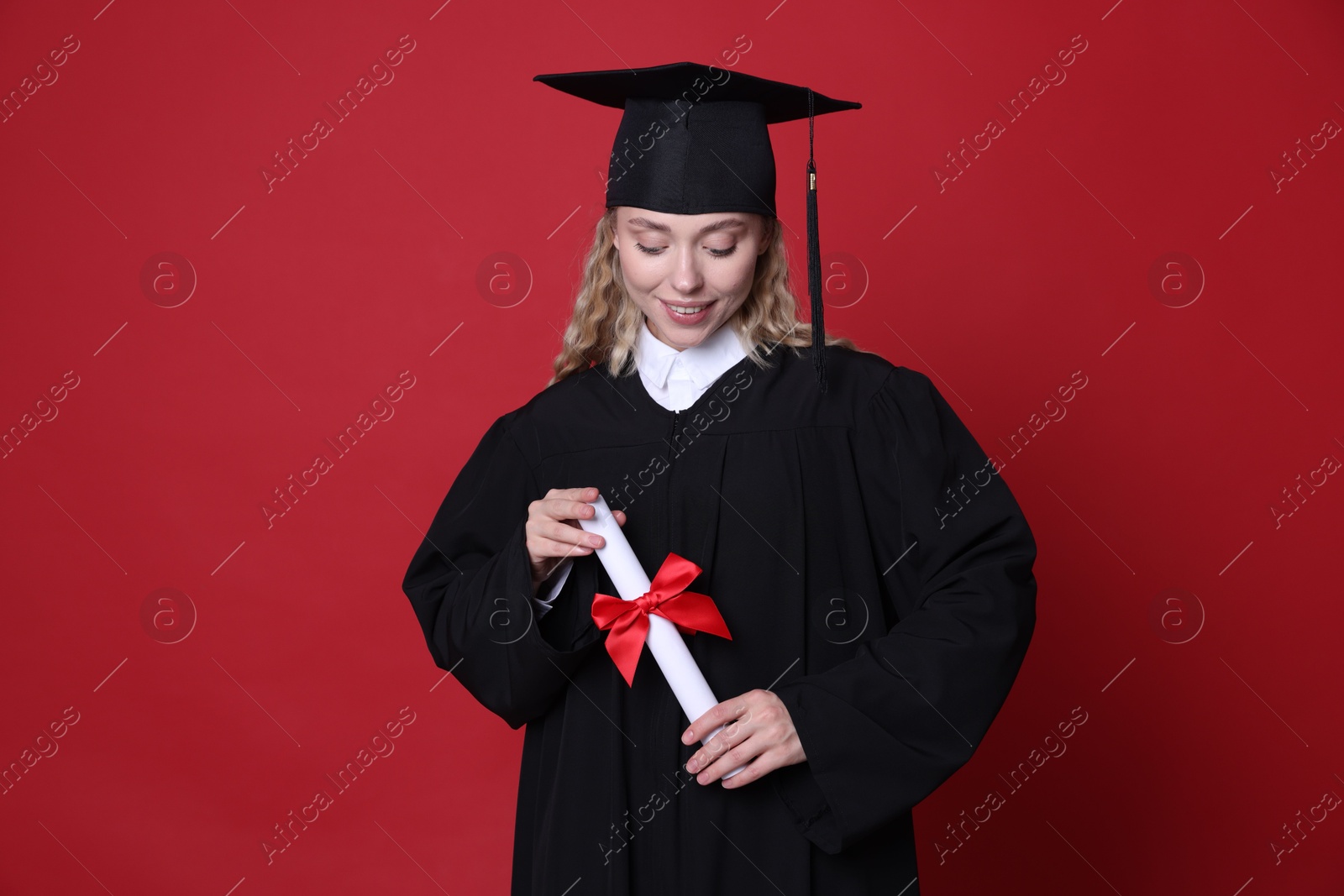 Happy student with diploma after graduation on red background Photo of Happy student with diploma after graduation on red background