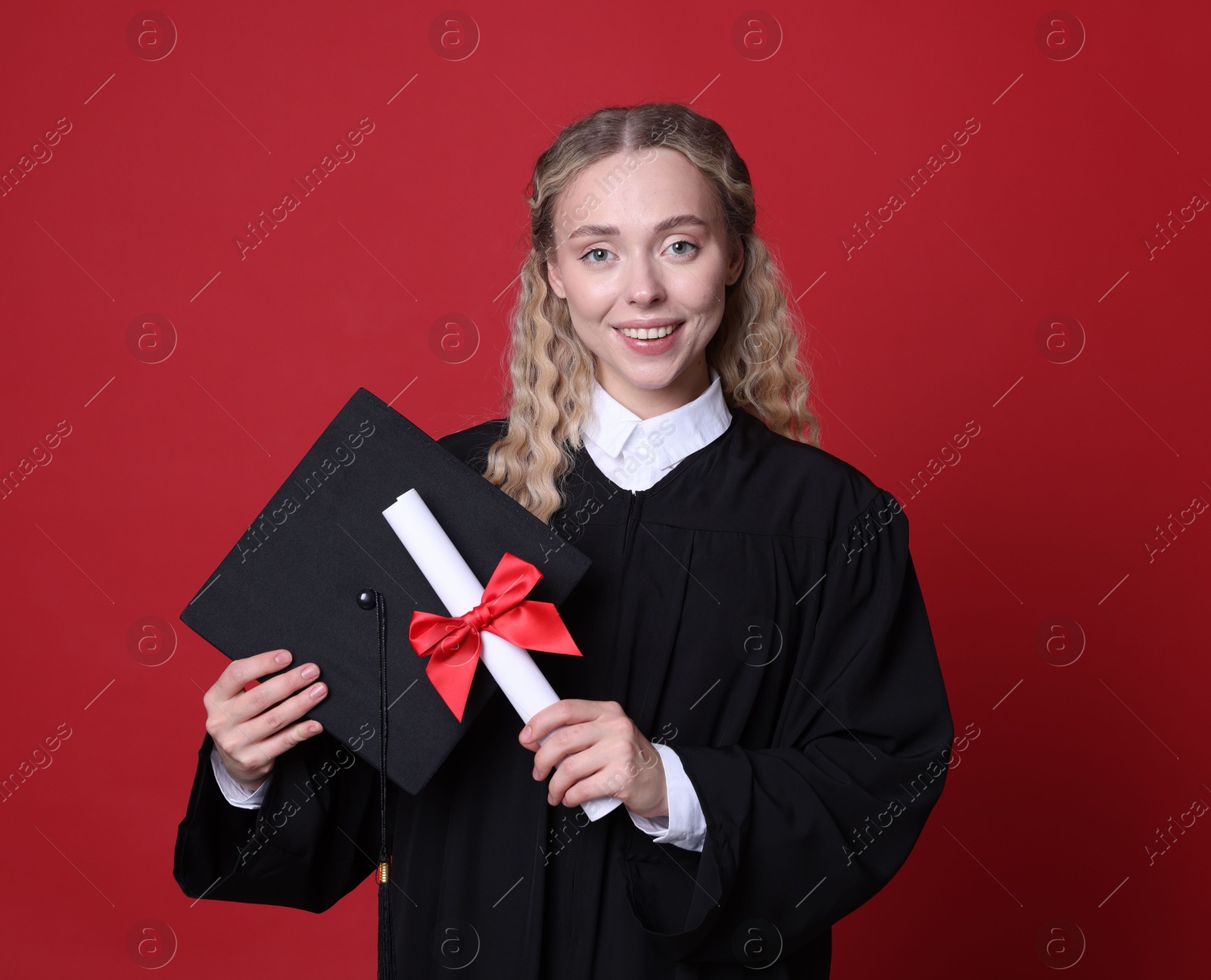 Happy student with diploma and mortarboard after graduation on red background Photo of Happy student with diploma and mortarboard after graduation on red background