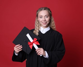 Photo of Happy student with diploma and mortarboard after graduation on red background