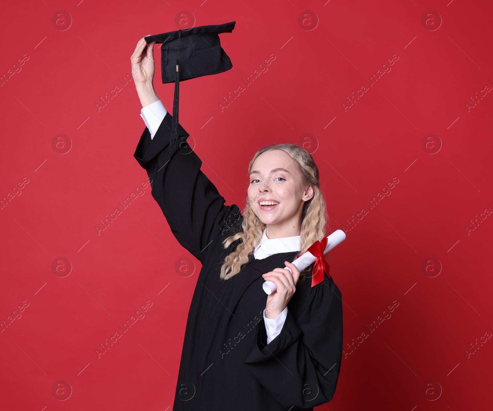 Happy student with diploma and mortarboard after graduation on red background Photo of Happy student with diploma and mortarboard after graduation on red background