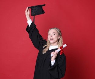 Photo of Happy student with diploma and mortarboard after graduation on red background