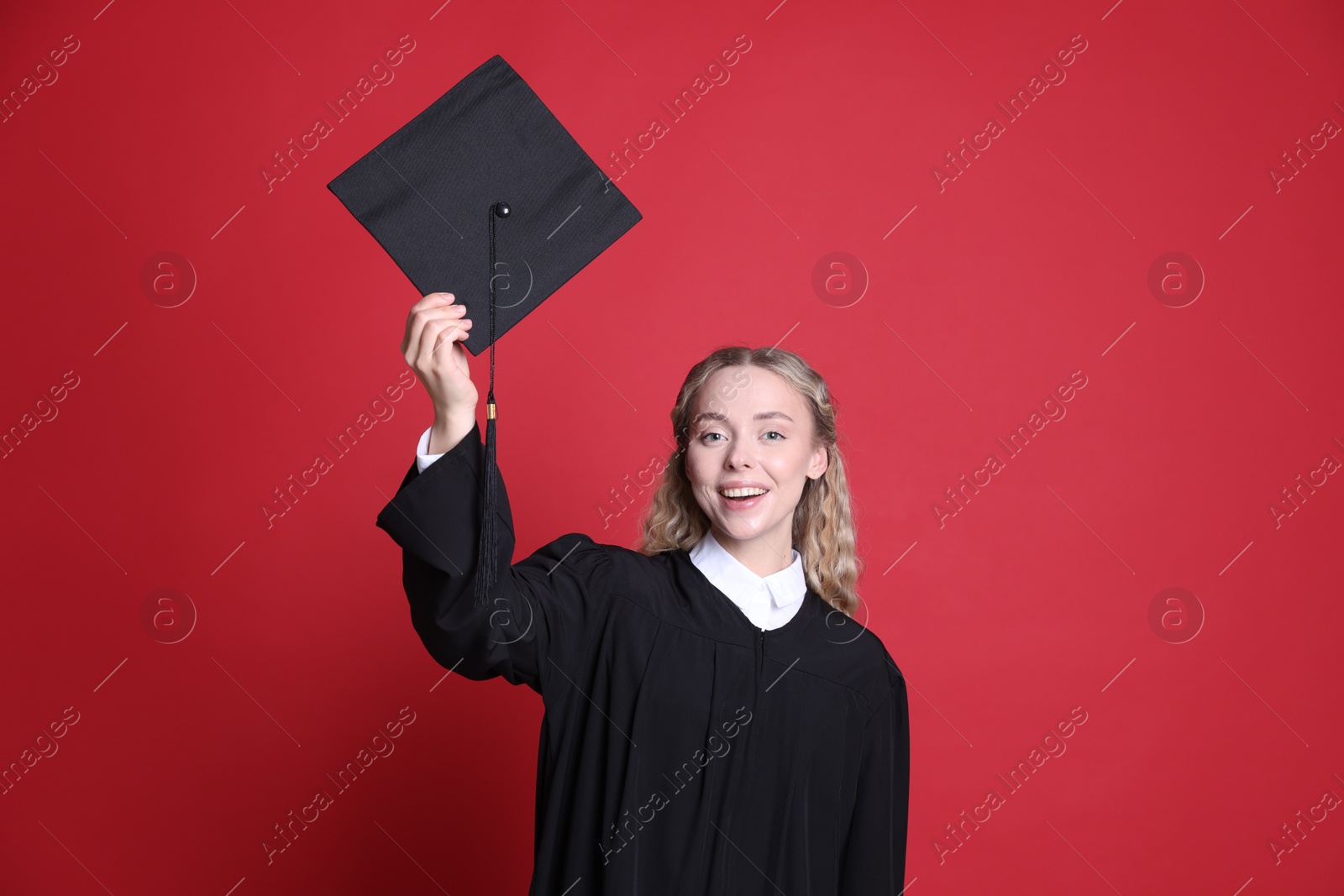 Happy student with mortarboard after graduation on red background Photo of Happy student with mortarboard after graduation on red background