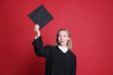 Photo of Happy student with mortarboard after graduation on red background