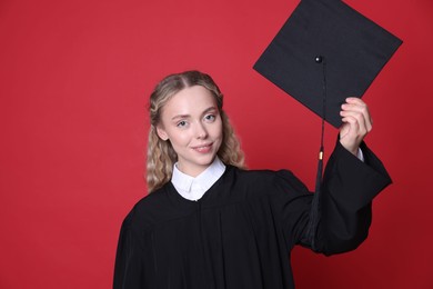 Photo of Happy student with mortarboard after graduation on red background