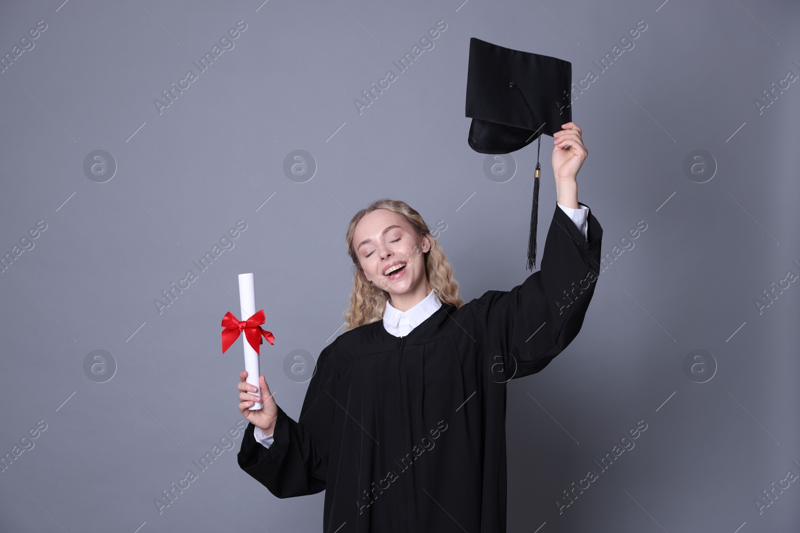 Happy student with diploma and mortarboard after graduation on grey background Photo of Happy student with diploma and mortarboard after graduation on grey background