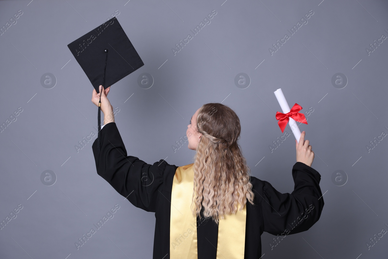 Student with diploma and mortarboard after graduation on grey background, back view Photo of Student with diploma and mortarboard after graduation on grey background, back view