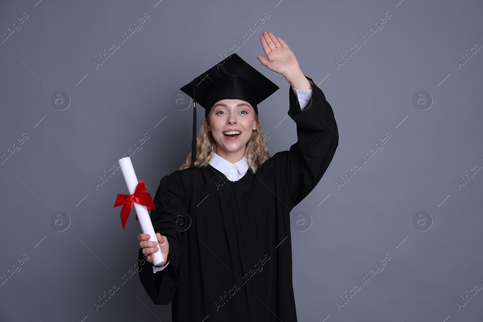 Happy student with diploma after graduation waving on grey background Photo of Happy student with diploma after graduation waving on grey background