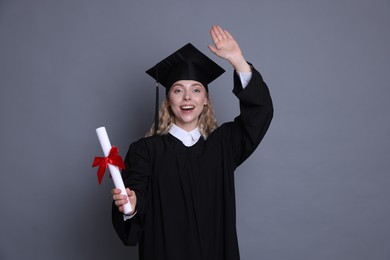 Photo of Happy student with diploma after graduation waving on grey background
