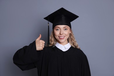 Photo of Happy student after graduation showing thumbs up on grey background