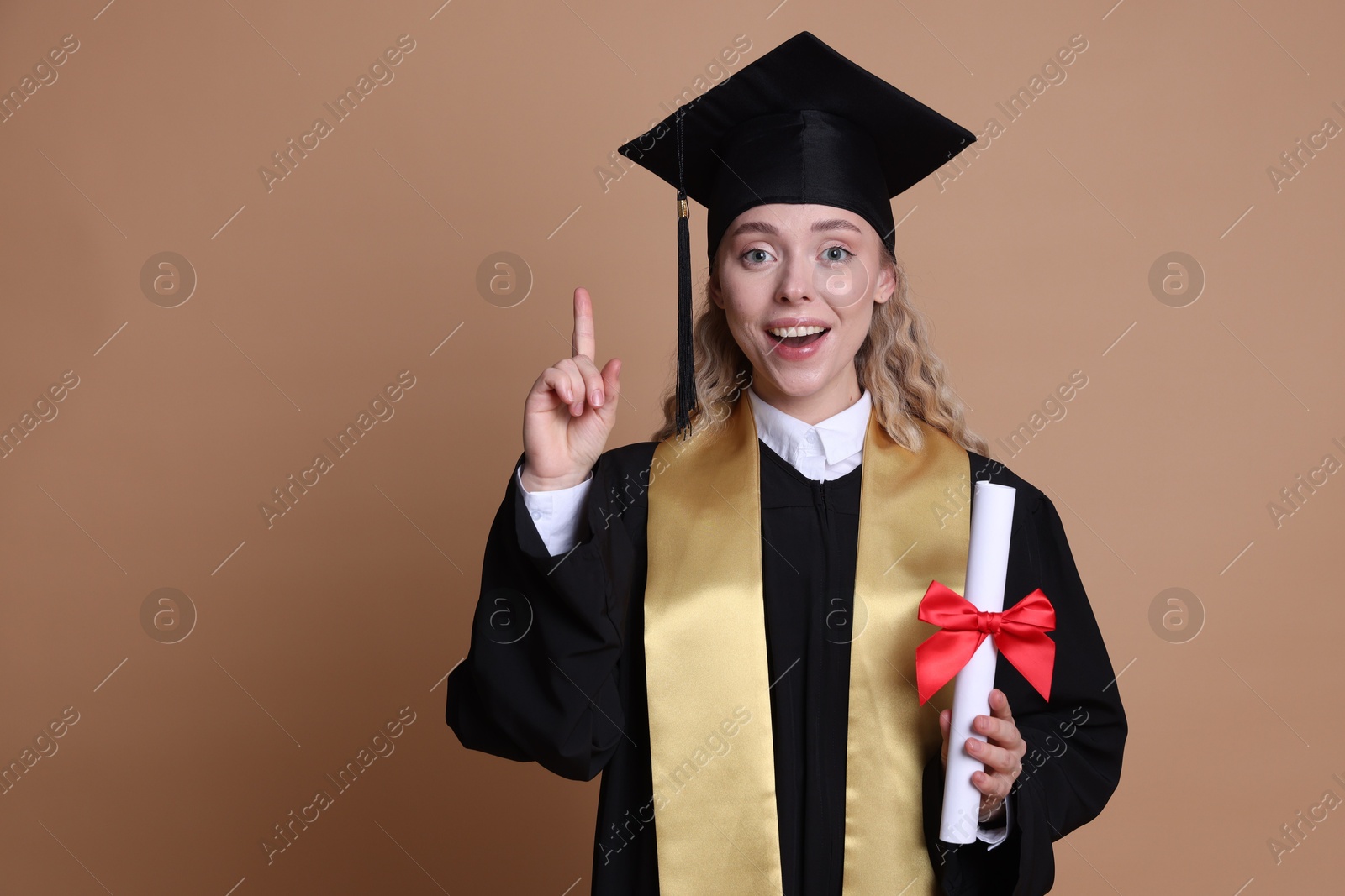 Happy student with diploma after graduation pointing upwards on beige background. Space for text Photo of Happy student with diploma after graduation pointing upwards on beige background. Space for text