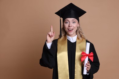 Photo of Happy student with diploma after graduation pointing upwards on beige background. Space for text