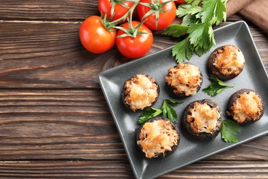 Photo of Delicious stuffed mushrooms with parsley and tomatoes on wooden table, flat lay. Space for text