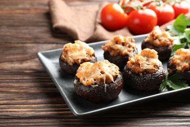 Photo of Delicious stuffed mushrooms with parsley and tomatoes on wooden table, closeup