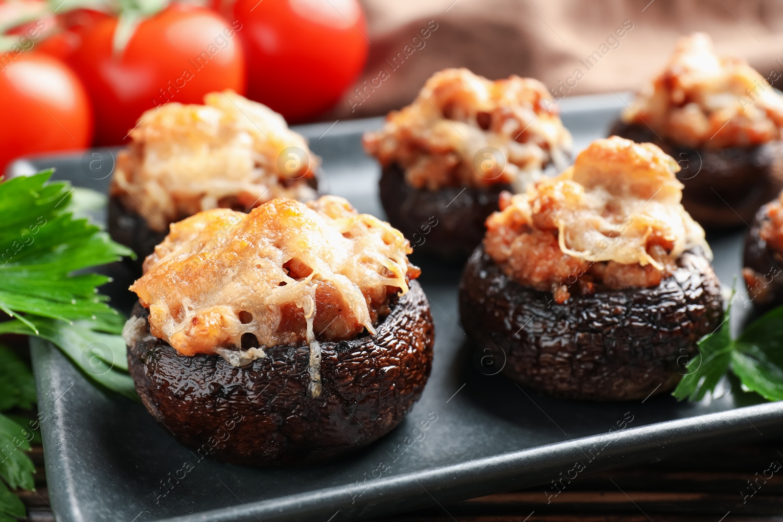 Delicious stuffed mushrooms with parsley and tomatoes on table, closeup Photo of Delicious stuffed mushrooms with parsley and tomatoes on table, closeup