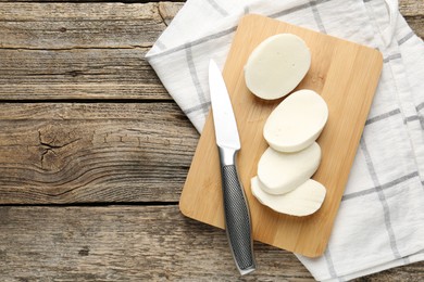 Photo of Cut mozzarella cheese and knife on wooden table, top view. Space for text