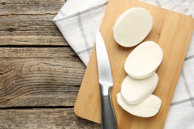 Photo of Cut mozzarella cheese and knife on wooden table, top view. Space for text