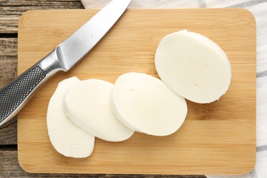 Photo of Cut mozzarella cheese and knife on wooden table, top view