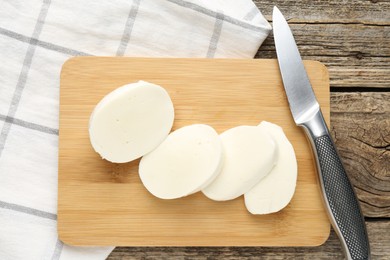 Photo of Cut mozzarella cheese and knife on wooden table, top view