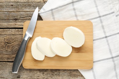 Photo of Cut mozzarella cheese and knife on wooden table, top view