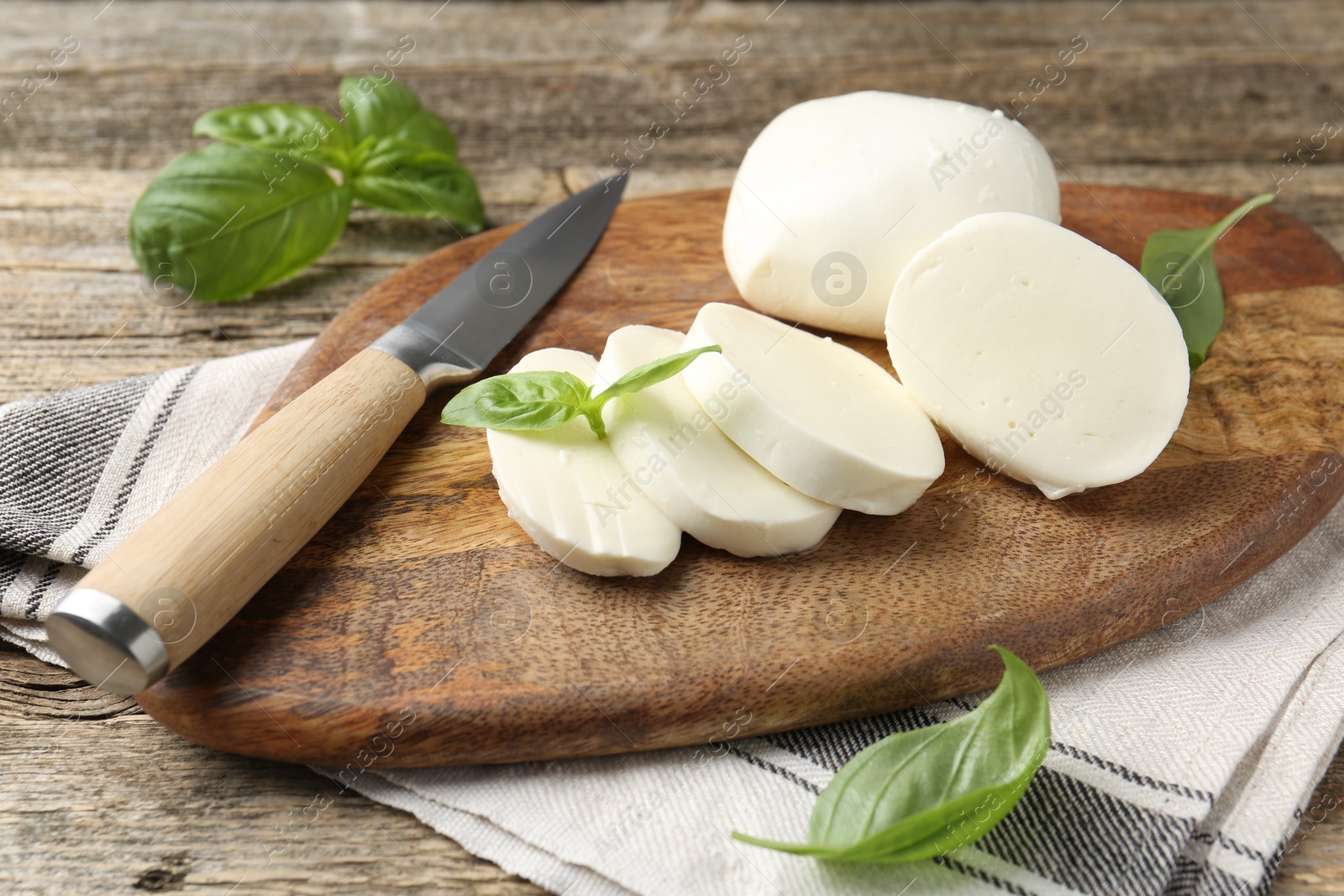Cut mozzarella cheese with basil and knife on wooden table, closeup Photo of Cut mozzarella cheese with basil and knife on wooden table, closeup