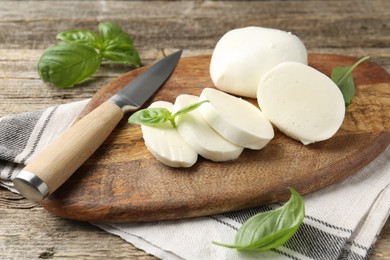 Photo of Cut mozzarella cheese with basil and knife on wooden table, closeup