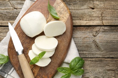 Photo of Cut mozzarella cheese with basil and knife on wooden table, flat lay. Space for text