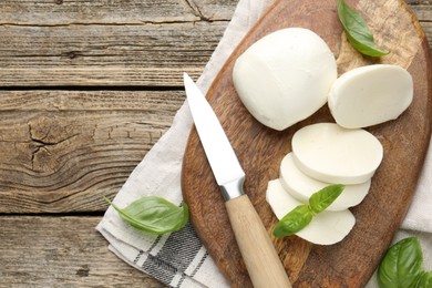 Photo of Cut mozzarella cheese with basil and knife on wooden table, flat lay. Space for text