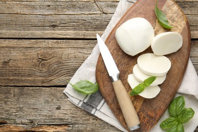 Photo of Cut mozzarella cheese with basil and knife on wooden table, flat lay. Space for text