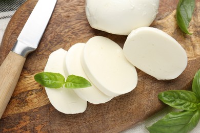 Photo of Cut mozzarella cheese with basil and knife on wooden table, flat lay