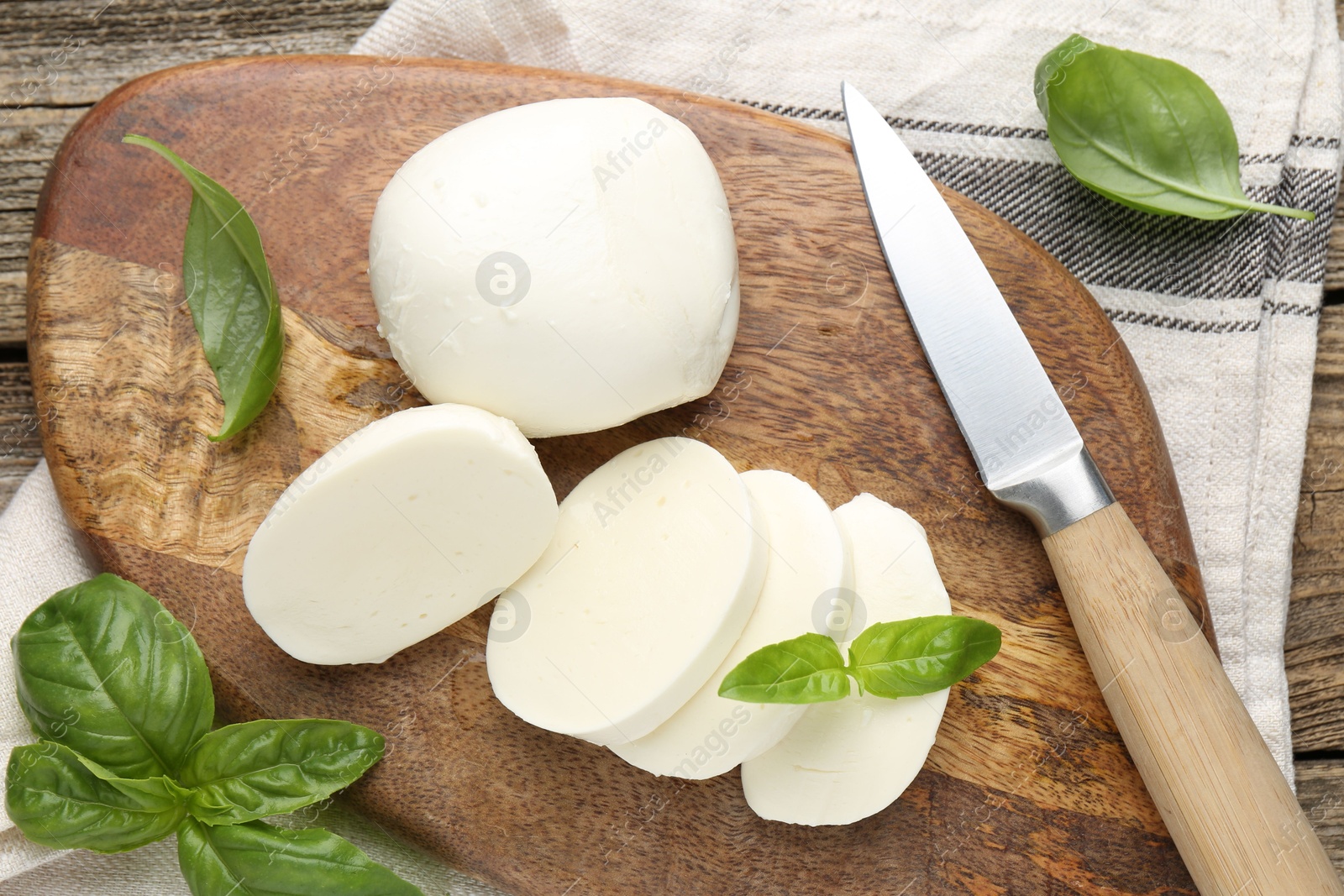 Cut mozzarella cheese with basil and knife on wooden table, flat lay Photo of Cut mozzarella cheese with basil and knife on wooden table, flat lay