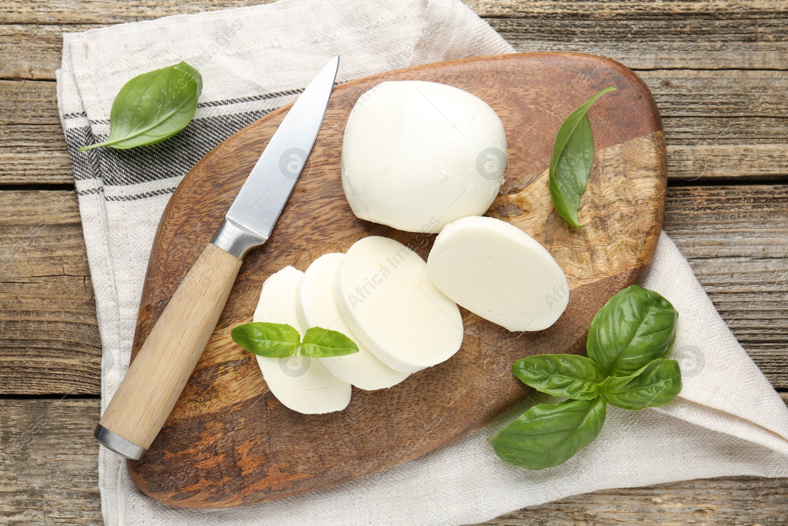 Cut mozzarella cheese with basil and knife on wooden table, flat lay Photo of Cut mozzarella cheese with basil and knife on wooden table, flat lay