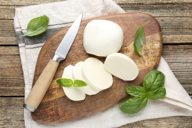 Photo of Cut mozzarella cheese with basil and knife on wooden table, flat lay