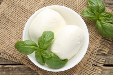 Photo of Tasty mozzarella cheese and basil on wooden table, top view