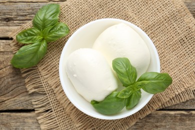 Photo of Tasty mozzarella cheese and basil on wooden table, top view