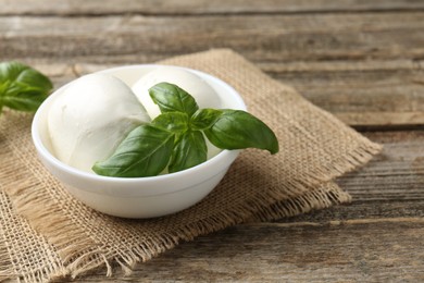 Photo of Tasty mozzarella cheese and basil on wooden table, closeup. Space for text