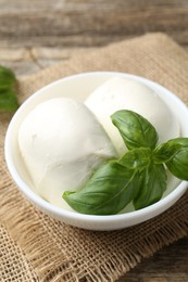Photo of Tasty mozzarella cheese and basil on wooden table, closeup