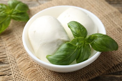 Photo of Tasty mozzarella cheese and basil on wooden table, closeup