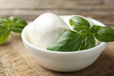 Photo of Tasty mozzarella cheese and basil on wooden table, closeup
