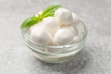 Photo of Mozzarella cheese balls and basil on light grey table, closeup