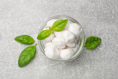 Photo of Mozzarella cheese balls and basil on light grey table, top view