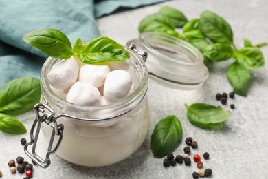 Photo of Mozzarella cheese balls with basil and peppercorns on light grey table, closeup