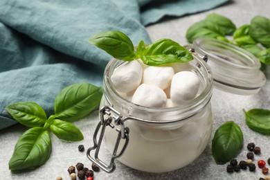 Photo of Mozzarella cheese balls with basil and peppercorns on light grey table, closeup