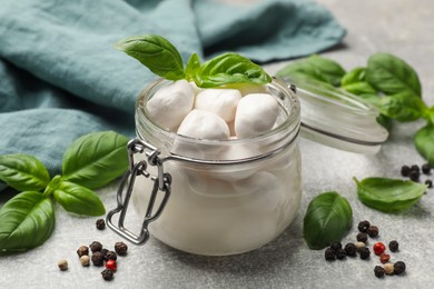 Photo of Mozzarella cheese balls with basil and peppercorns on light grey table, closeup