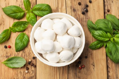Photo of Mozzarella cheese balls with basil and peppercorns on wooden table, flat lay
