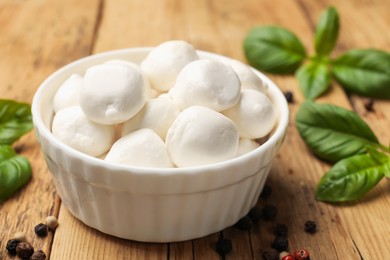 Photo of Mozzarella cheese balls with basil and peppercorns on wooden table, closeup