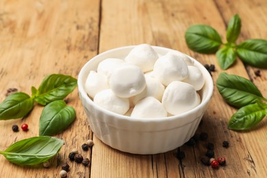 Photo of Mozzarella cheese balls with basil and peppercorns on wooden table, closeup